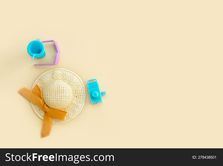 Sunglasses, straw hat, toy camera and toy glass with a straw on a pale beige background, vacation content from copy space