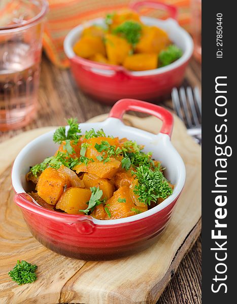 Pumpkin baked in a tomato sauce with garlic and herbs on a wooden board