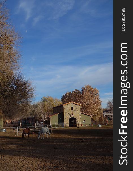 This a prototypical farm scene: pastoral with a barn, horses grazing, a blue sky, and a day-time moon. This a prototypical farm scene: pastoral with a barn, horses grazing, a blue sky, and a day-time moon.