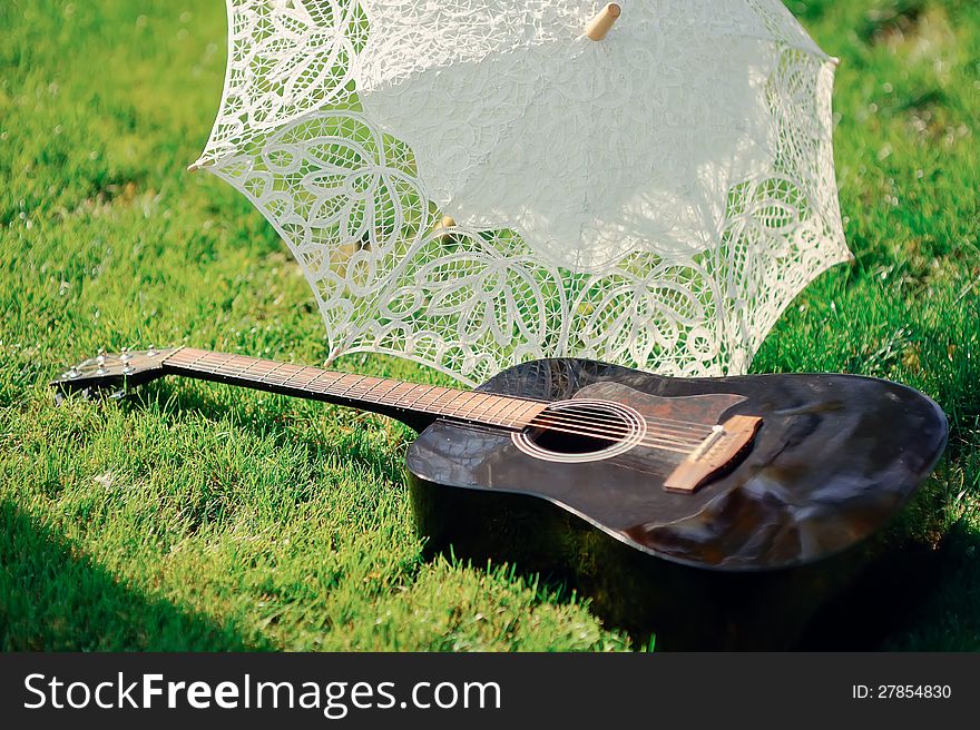 White lacy umbrella and a guitar lying on green grass. White lacy umbrella and a guitar lying on green grass