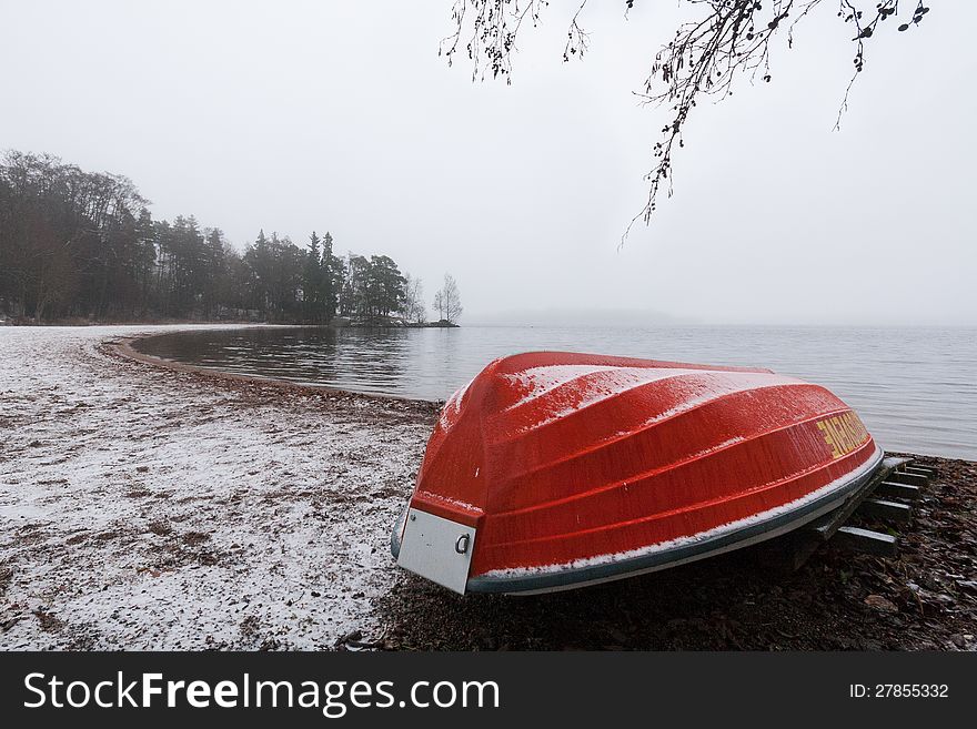 Red rowboat upside down at a snowy beach on a grey day