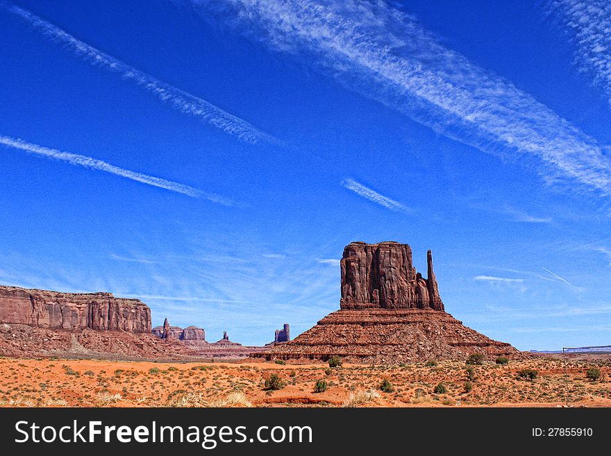 The red rock mountains and outcroppings of Monument Valley, Arizona are seen against a blue sky streaked with white clouds.