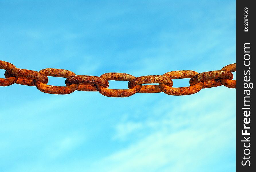 Old rusty chain hanging alone against a blue sky