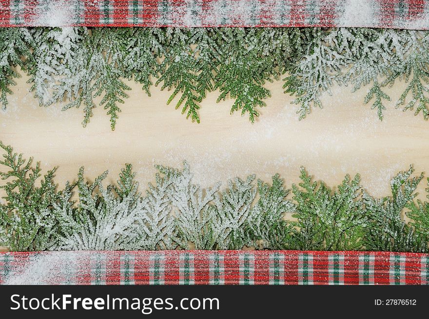Conifer branches on the wooden light background with plaid red ribbon. Conifer branches on the wooden light background with plaid red ribbon