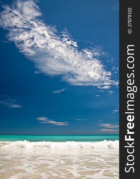Portrait view of turquoise blue sea with breaking wave with a brilliant blue sky featuring a white textured cloud. Portrait view of turquoise blue sea with breaking wave with a brilliant blue sky featuring a white textured cloud.