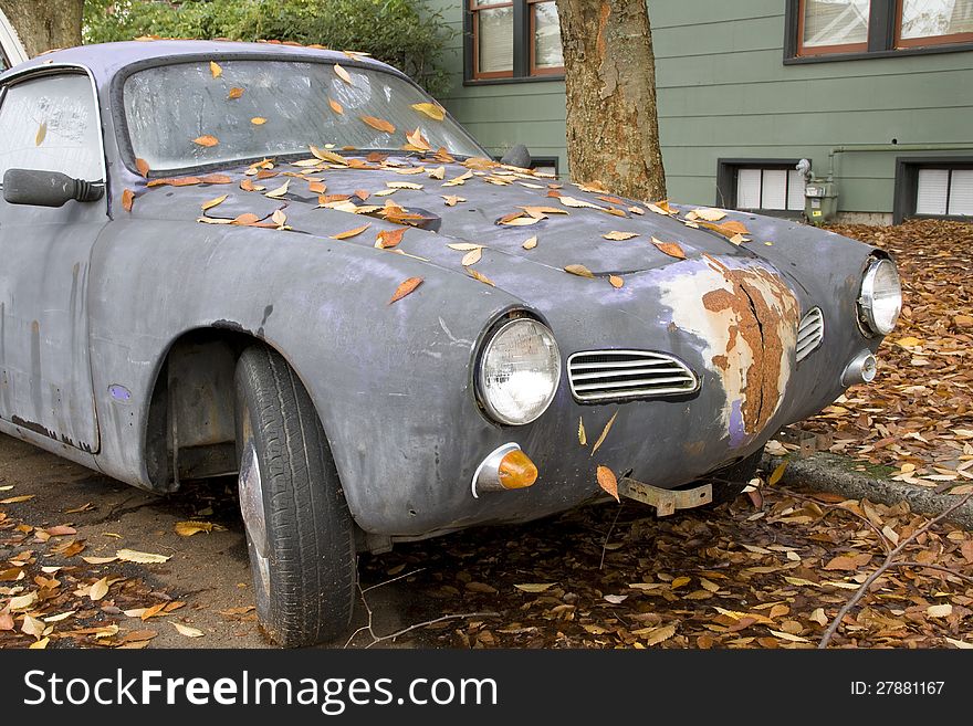 An old and rusty sport car with falling leaves. An old and rusty sport car with falling leaves.