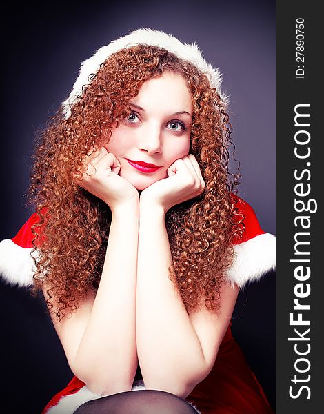 Pretty curly girl in a Santa suit on a dark background