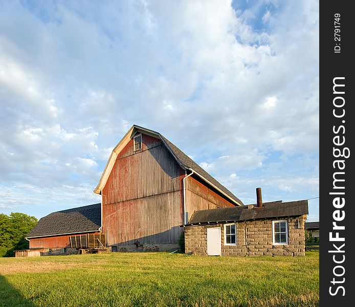 Faded red barn at sunset, with green grass in the foreground and a dramatic sky background. Faded red barn at sunset, with green grass in the foreground and a dramatic sky background