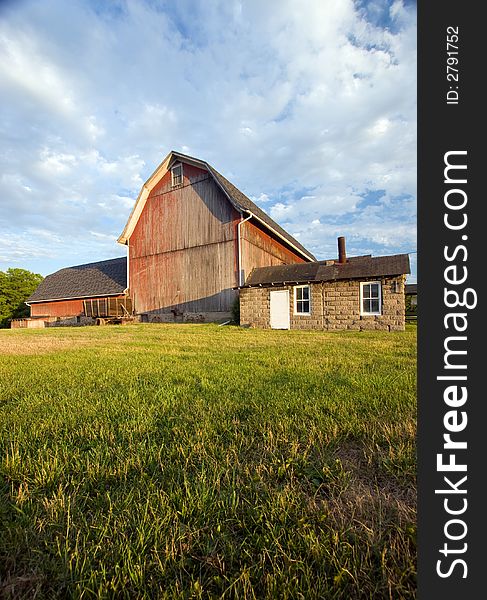 Faded red barn at sunset, with green grass in the foreground and a dramatic sky background. Faded red barn at sunset, with green grass in the foreground and a dramatic sky background