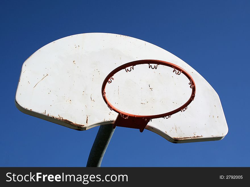 A playground basketball hoop against a blue sky.