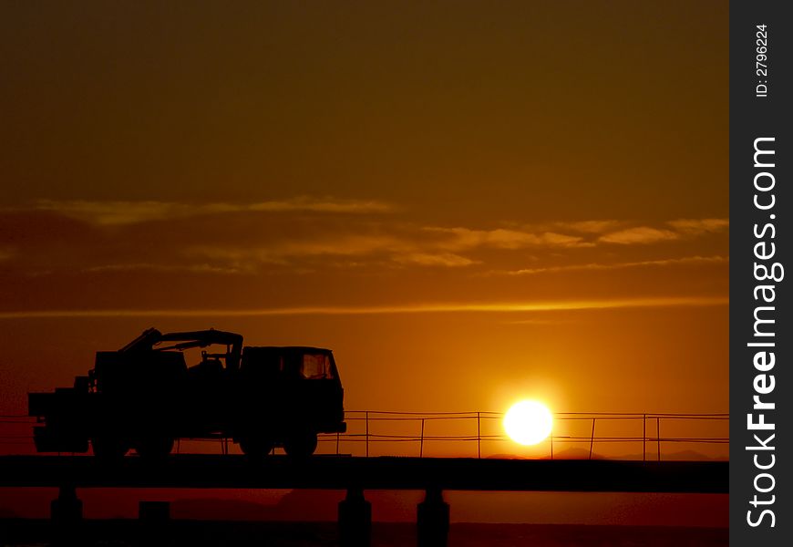 Red sunset with truck silhouette on a pier in progress. Red sunset with truck silhouette on a pier in progress