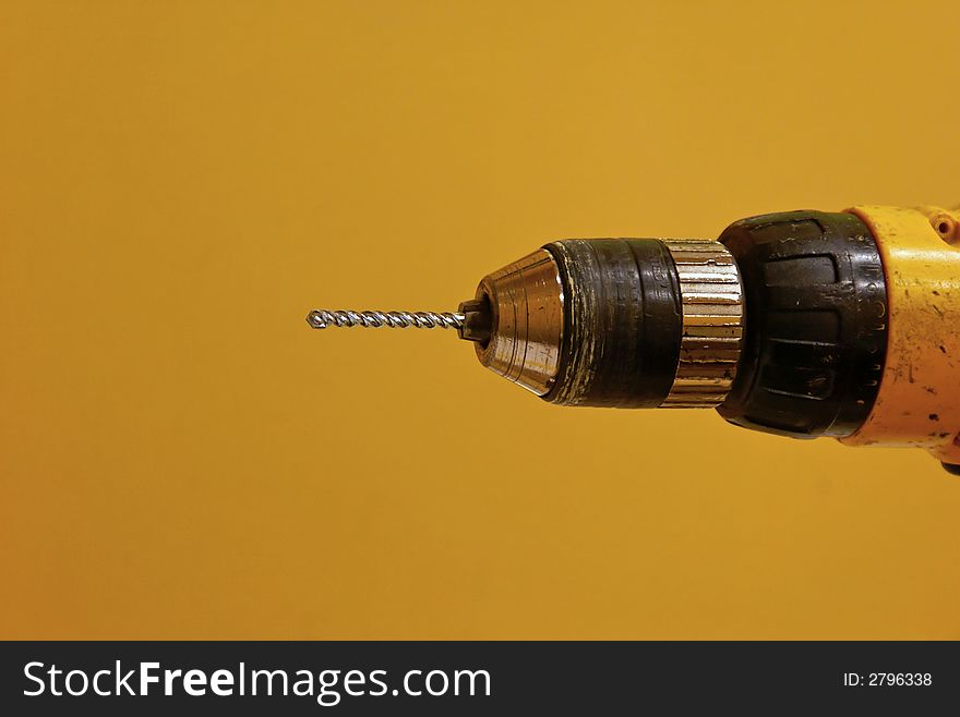 Old yellow drill with new cement drill bit against yellowish background. Old yellow drill with new cement drill bit against yellowish background