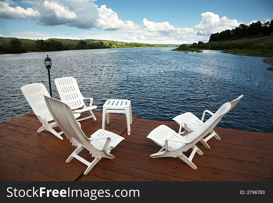 Five white armchairs and table on coast of a reservoir