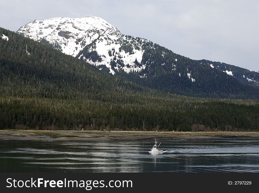 The small fishing-boat is going the channel with snow-covered mountains in a background in Juneau, Alaska. The small fishing-boat is going the channel with snow-covered mountains in a background in Juneau, Alaska.