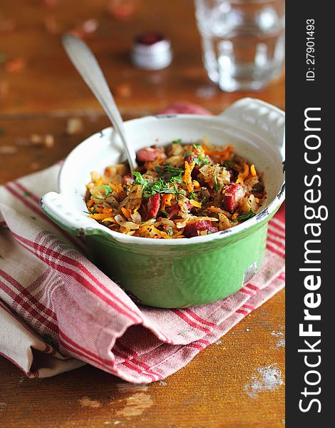 Stewed cabbage with sausages, carrots and lentil in a green sauce pan on a kitchen towel. Stewed cabbage with sausages, carrots and lentil in a green sauce pan on a kitchen towel