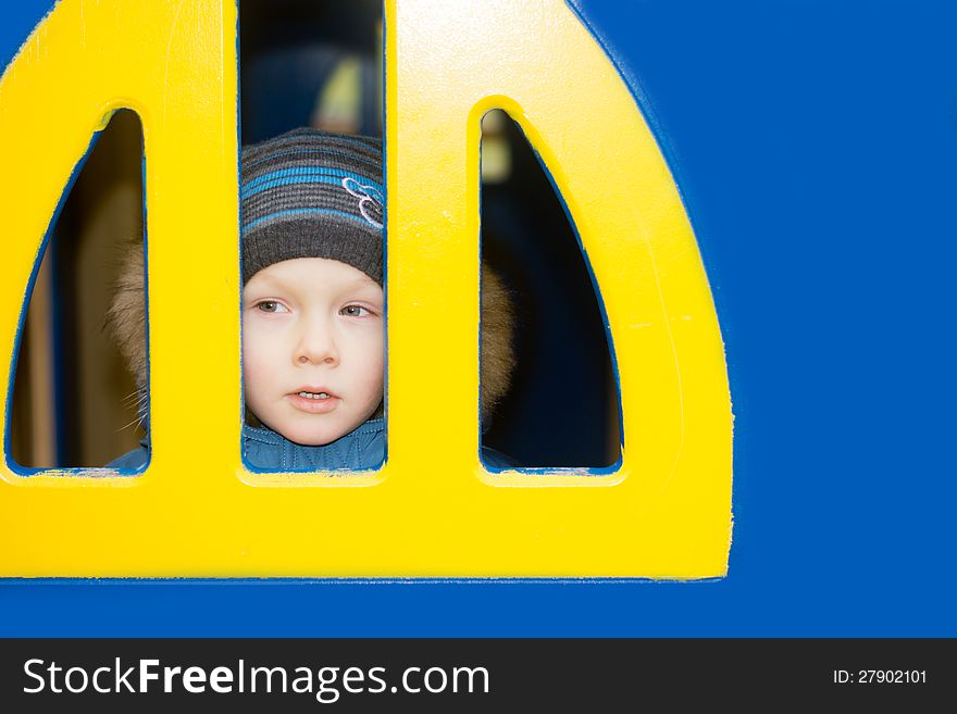 A kid looking from a yellow window on blue wall. A kid looking from a yellow window on blue wall.