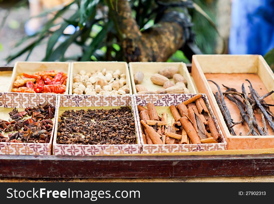 Trays of dried spaces and herbs for sale on a market stall including bark cinnamon, chillies and vanilla pods