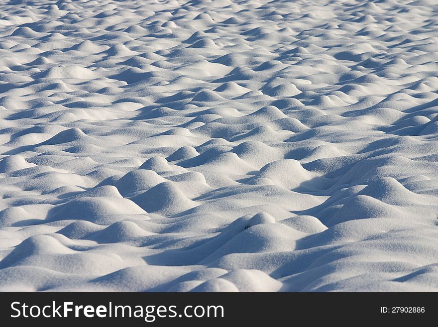 Soft and bright dunes of snow in a country field with shadows