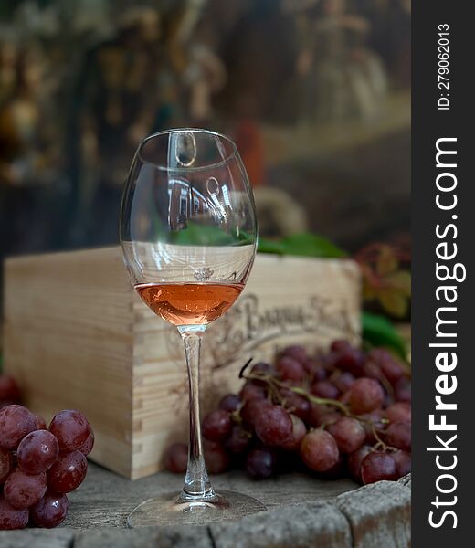 A Glass Of Rose Wine On A Wooden Surface In Front Of Grapes