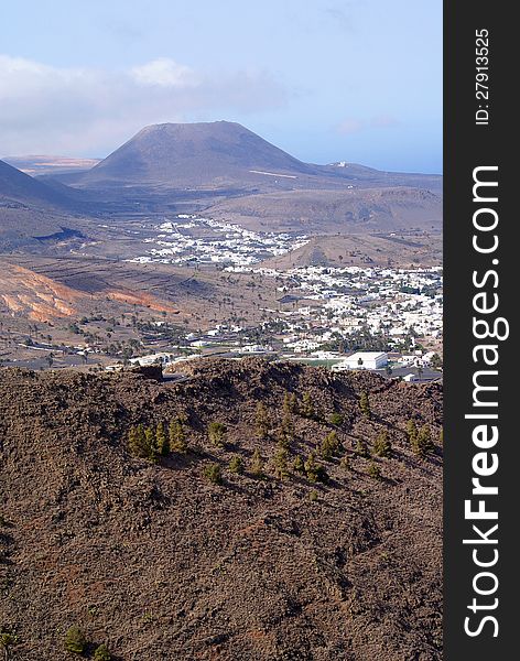 View of a valley with white houses and palm trees and mountains on the island of Lanzarote against blue sky. View of a valley with white houses and palm trees and mountains on the island of Lanzarote against blue sky