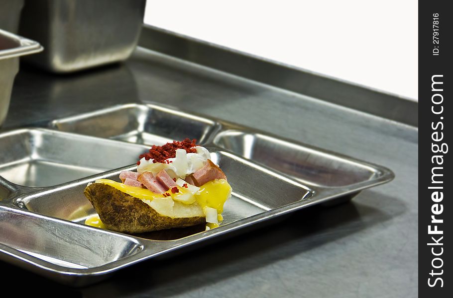Baked potato with toppings on metal tray in cafeteria. Baked potato with toppings on metal tray in cafeteria