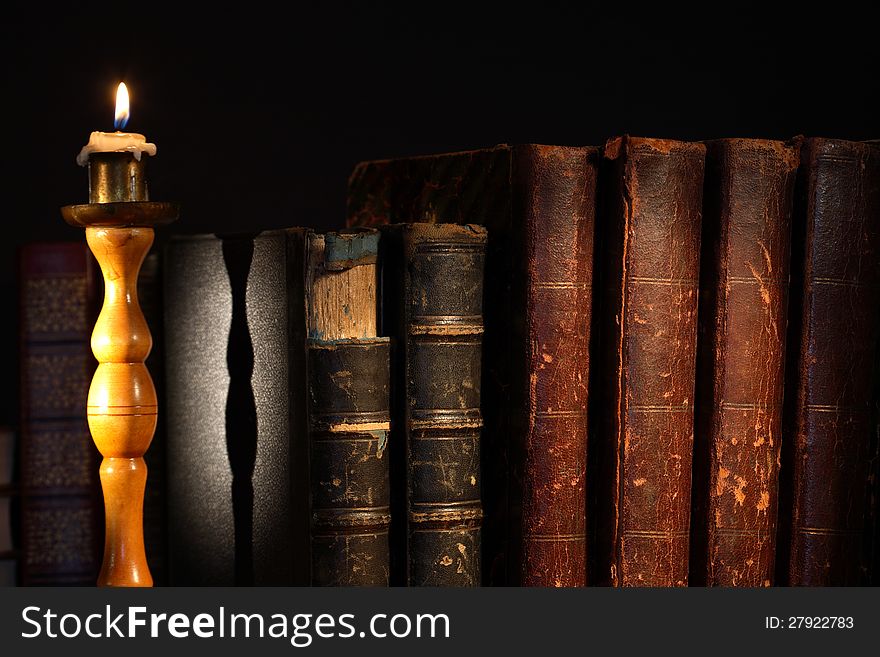 Ancient books in a row near lighting candle on dark background. Ancient books in a row near lighting candle on dark background