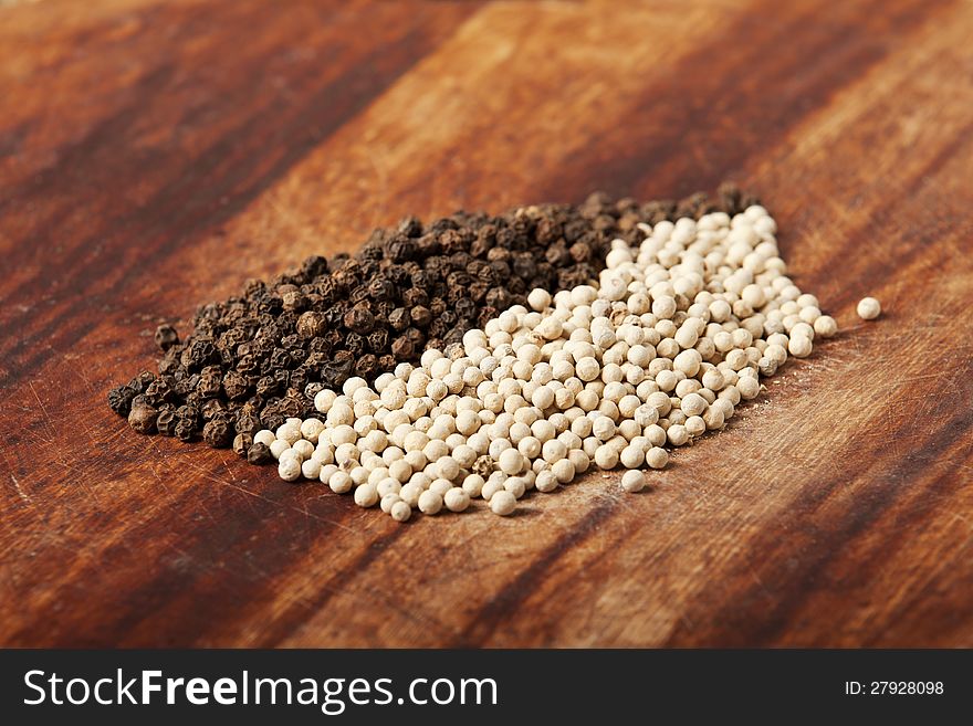 Black and white pepper on wood background