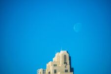 A Bright White Crescent Moon Rises Over A Blocky Tan Stone High Rise Skyscraper Building With A True Blue Sky Royalty Free Stock Photography