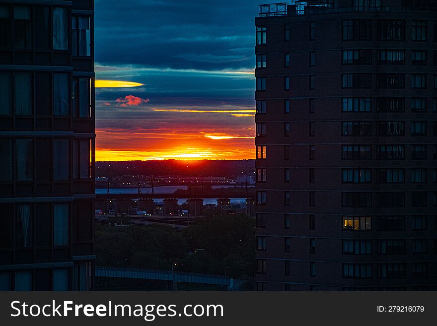 Vibrant orange and red sunrise against dark aquamarine navy blue clouds between two high-rise urban buildings on the upper east side of Manhattan, New York.