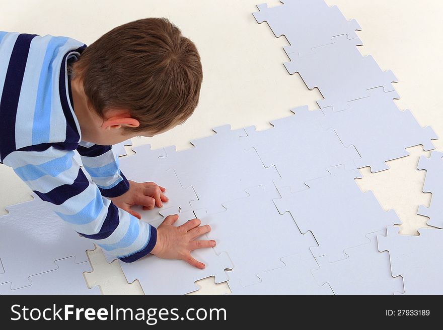 Boy laying an white elements of a jigsaw puzzle on the white background. Boy laying an white elements of a jigsaw puzzle on the white background