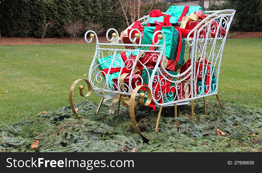 Pretty white and gold sleigh filled with colorful wrapped gifts and set on loose pine branches welcomes the season of christmas. Pretty white and gold sleigh filled with colorful wrapped gifts and set on loose pine branches welcomes the season of christmas.