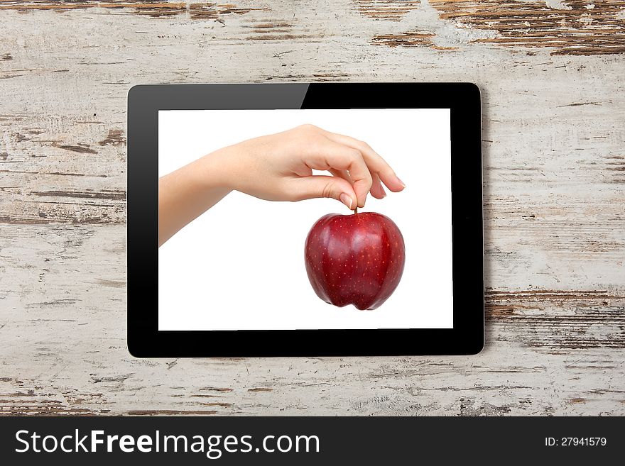 Tablet computer with the hand and a red apple on the screen on a background of wood. Tablet computer with the hand and a red apple on the screen on a background of wood