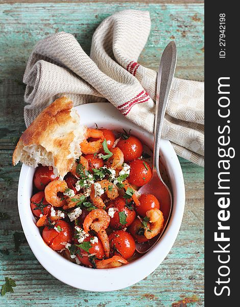 Baked shrimps and cherry tomatoes with feta cheese and fresh parsley in a baking dish with bread