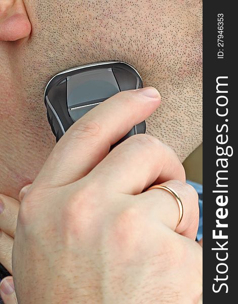 Man shaves his cheek using electric shaver. Macro closeup. Man shaves his cheek using electric shaver. Macro closeup