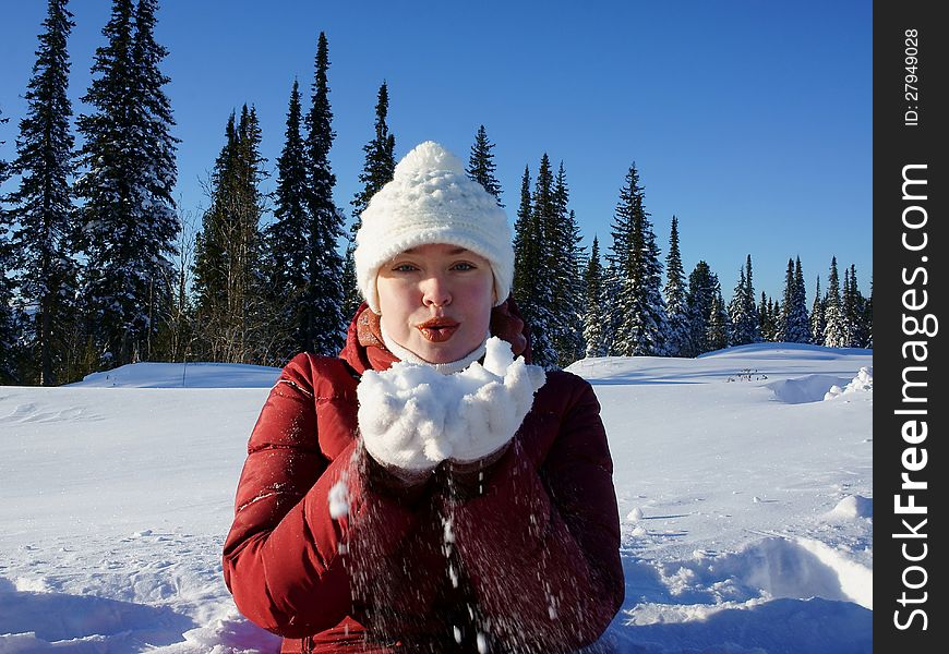 Girl clad in a red jacket and white hat, holds the snow on the hands of winter forest. Girl clad in a red jacket and white hat, holds the snow on the hands of winter forest.