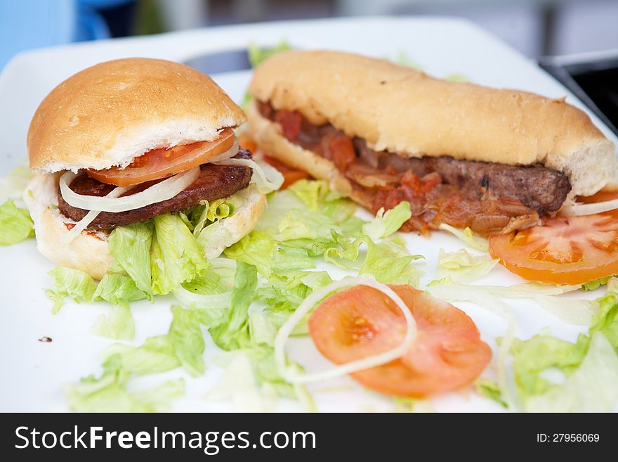 Beef hamburger and hotdog on white plate with garnish