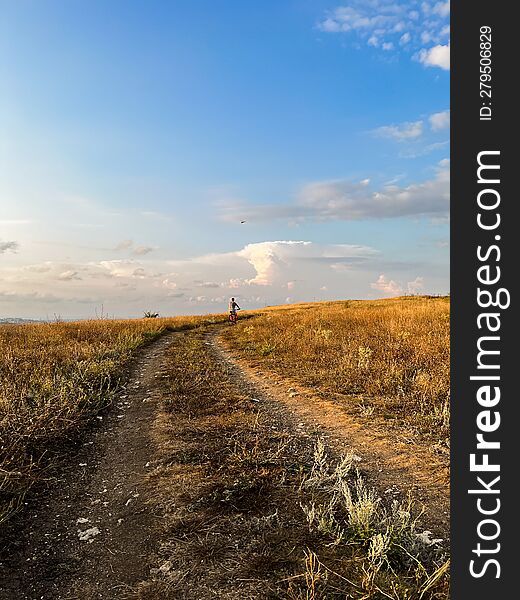 A path in the steppe on a hill. Someone is riding a bicycle on the horizon. Evening sky.  An empty steppe field.