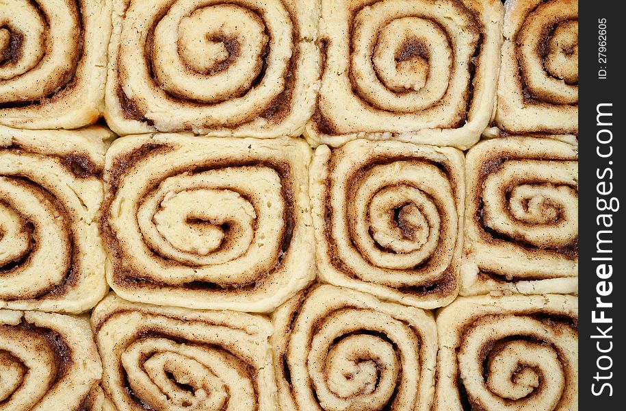 Twelve cinnamon buns in a rectangular tray showing a pattern of spiral swirls and straight edges