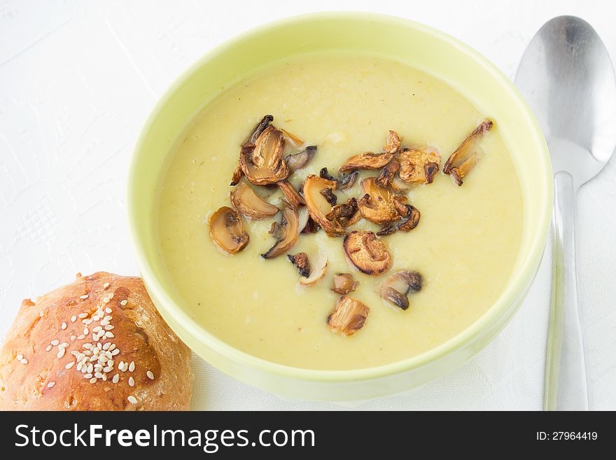 Leek mashed soup with fried sliced mushrooms in the green bowl with bun and spoon. White background.