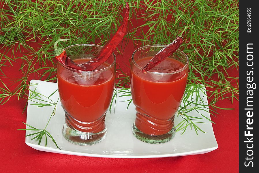 Two glasses of tomato juice with leaves on a white background