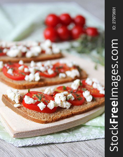 Cherry Tomato and Feta bread slices with Thyme on a wooden cutting board. Cherry Tomato and Feta bread slices with Thyme on a wooden cutting board