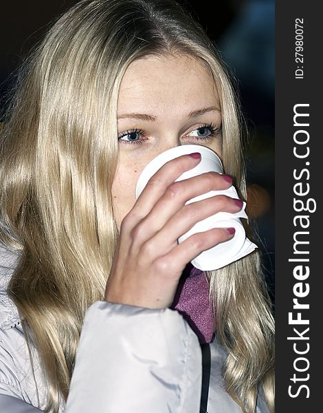 Blue-eyed blonde with long hair drinks from plastic glass. Blue-eyed blonde with long hair drinks from plastic glass