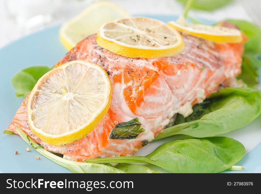 Baked salmon fillet with lemon and spinach on a plate closeup. Baked salmon fillet with lemon and spinach on a plate closeup