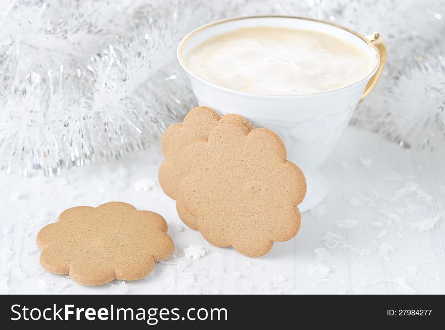 Ginger biscuits, a cup of cappuccino, a Christmas tinsel on a white table, horizontal. Ginger biscuits, a cup of cappuccino, a Christmas tinsel on a white table, horizontal