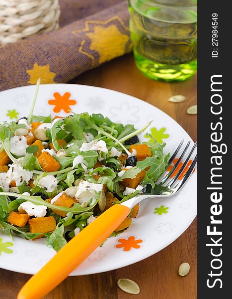 Salad with pumpkin, feta and arugula on a plate closeup vertical