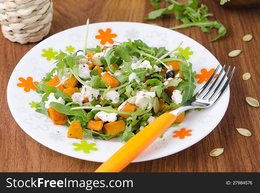 Salad with pumpkin, feta and arugula on a plate closeup