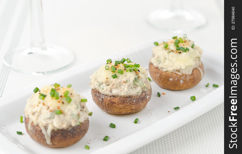 Stuffed mushrooms, baked with cheese and herbs on white dish, selective focus. Stuffed mushrooms, baked with cheese and herbs on white dish, selective focus