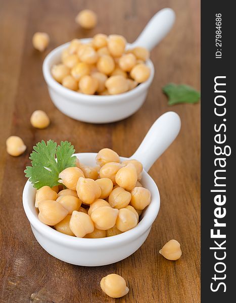 Two cups of boiled chickpeas on a wooden background