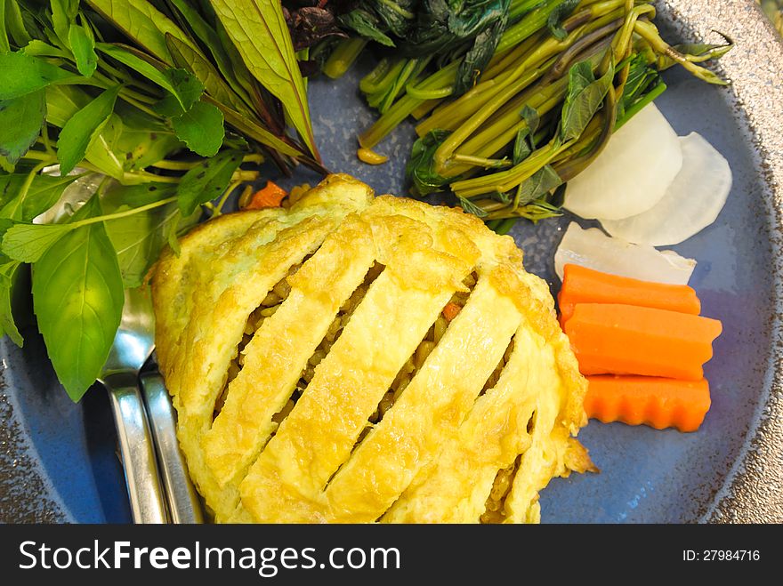 Brown fried rice with egg and fresh vegetable in blue ceramic plate