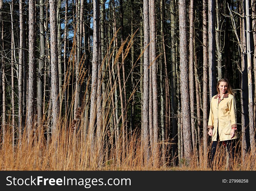 Pretty blonde-haried lady dressed in leather jacket standing out in a field of tall grass and pine trees. Pretty blonde-haried lady dressed in leather jacket standing out in a field of tall grass and pine trees.